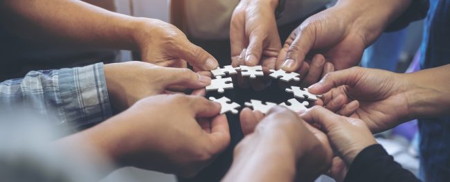 Closeup image of many people hands holding a jigsaw puzzle in circle together